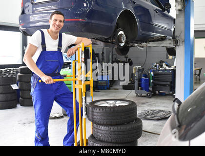 Reifenwechsel in der Werkstatt - Porträt Mechaniker mit Stack von Reifen für den Austausch Stockfoto