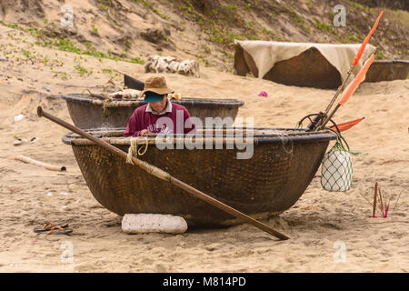 Eine vietnamesische Fischer empfiehlt sein Netz während der Sitzung in einer Runde coracle Boot am Strand von Hoi An, Vietnam Stockfoto