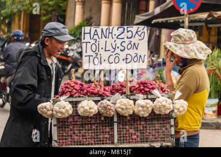 Ein Mann schiebt seinen Handwagen mit Zwiebeln und Knoblauch für den Verkauf auf der Straße in Hoi An, Vietnam Stockfoto