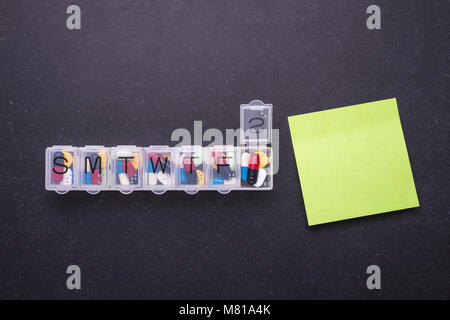 7 Tag Kunststoff Pille Veranstalter und Grünbuch Hinweis auf dunklen Tisch Hintergrund. Ansicht von oben Stockfoto