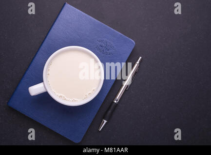 Milch in weißem Glas und Notiz Buch auf schwarzen Steintisch Hintergrund. Ansicht von oben und Studio shot Stockfoto