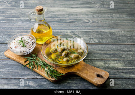 Olivenöl in Gräfin und Oliven mit Gewürzen und duftenden Kräutern auf einem Holz- Hintergrund. Stockfoto