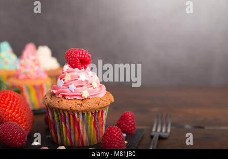 Selbst gebackene Muffins mit bunten Zuckerguss und Frucht auf eine Steintafel Stockfoto