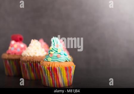 Selbst gebackene Muffins mit bunten Zuckerguss und Obst Stockfoto