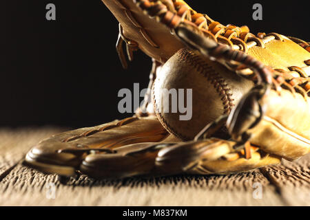 Nahaufnahme Bild eines alten verwendet Baseball und Baseball Handschuh auf hölzernen Tisch in schwarzer Hintergrund Stockfoto