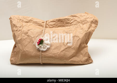 Geschenk in Zerknitterten vintage Recycling braunes Papier mit dem Bindfaden und die angeschlossenen Dekoration mit roten Beeren auf weißem Hintergrund Stockfoto