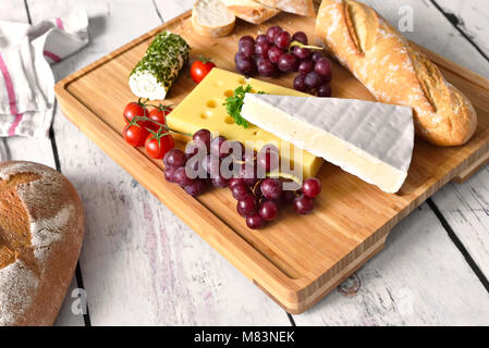 Käseplatte, Variation von frischen Käse, Camembert, Frischkäse und Leerdamer Käse auf einem hölzernen Schneidebrett. Frisches Brot oder Baguette, Abendessen Szene. Stockfoto