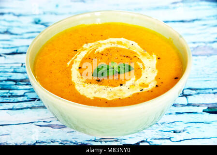 Schüssel mit Kürbis Suppe und Sahne auf einem Holztisch. Orange Suppe mit Sahne und Basil leaf. Gourmet Szene mit rustikalen Tisch. Stockfoto