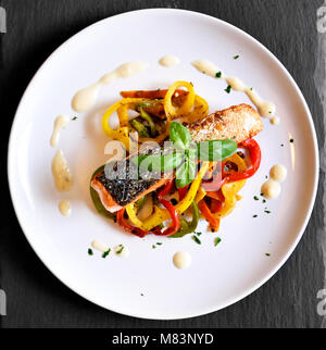 Leckere Lachsfilet und rote Paprika Gemüse auf einem weißen Teller. Gesunde Mahlzeit auf einer Schiefertafel Platte, mit Basil leaf eingerichtet. Gourmet Szene. Stockfoto