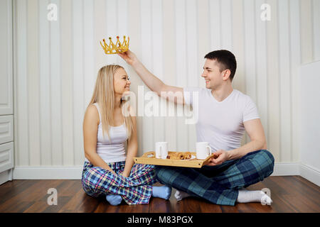 Ein glückliches Paar in den Schlafanzügen sitzen auf dem Boden in einem Zimmer gegen eine gestreifte Wand Hintergrund. Stockfoto