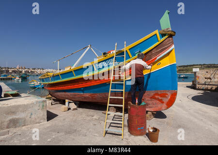 Mann malen bunte Fischerboot im Hafen von Marsaxlokk, Malta, unter blauen, wolkenlosen Himmel. Stockfoto