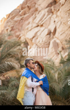 Junges Paar in der Ukraine Flagge gewickelt sind, Küssen in Canyon gegen den Hintergrund der Palmen und Felsen. Nahaufnahme. Stockfoto