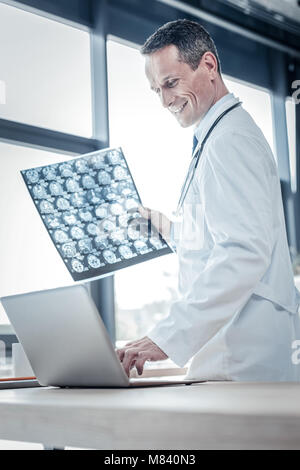 Zufrieden angenehm Arzt auf den Laptop und Holding x-ray-Scan. Stockfoto