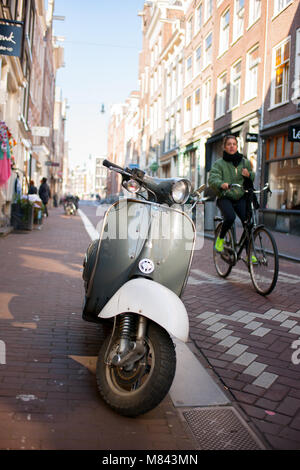 Retro alte Roller auf der Amsterdamer Straße mit Frau Radfahrer vorbei geparkt. Stockfoto