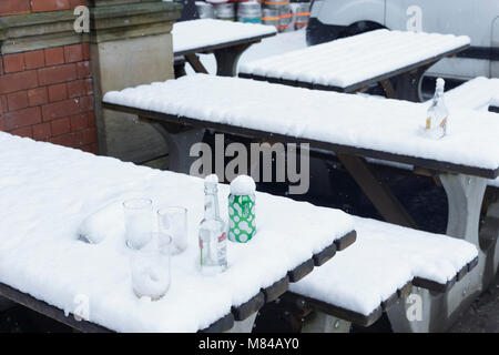 Leere Bierflaschen und Gläser im Schnee, auf schneebedeckten Bank außerhalb' der Bibliothek 'pub, Woodhouse Lane, Leeds, England. 8. März 2018 Stockfoto