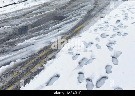 Teilweise sichtbar doppelten gelben Linien unter Schlamm, Schnee, Schneeregen und Schnee auf der Straße, Woodhouse, Leeds, England. 8. März 2018 Stockfoto