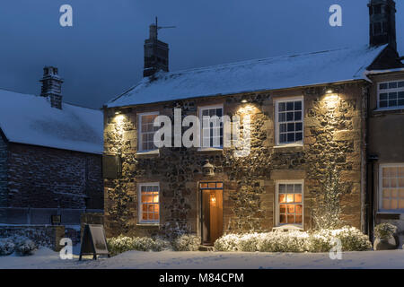 Einladende Village Inn an einem verschneiten Winterabend, Bamburgh, Northumberland, England. Winter (Februar) 2018. Stockfoto