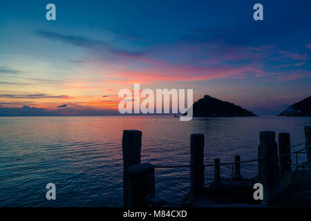 Sonnenuntergang auf dem Meer, mit Blick auf Koh Nang Yuan von Ko Tao, holzstäbchen eines Piers im Vordergrund, und ein rosa orange gelb und blauer Himmel Stockfoto