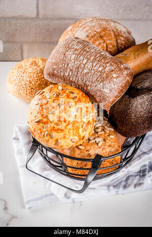 Auswahl an frischen, hausgemachten Korn Brot, in einem Metallkorb, weißem Marmor Background Copy space Stockfoto