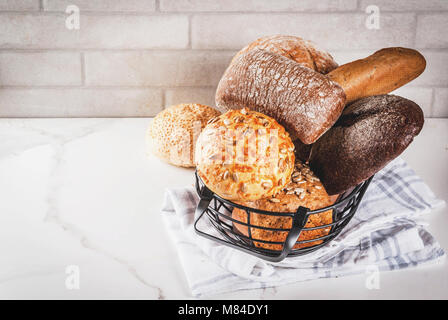 Auswahl an frischen, hausgemachten Korn Brot, in einem Metallkorb, weißem Marmor Background Copy space Stockfoto
