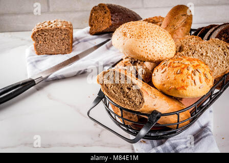 Auswahl an frischen, hausgemachten Korn Brot, in einem Metallkorb, weißem Marmor Background Copy space Stockfoto