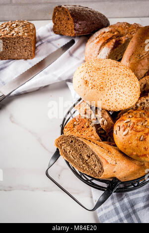 Auswahl an frischen, hausgemachten Korn Brot, in einem Metallkorb, weißem Marmor Background Copy space Stockfoto