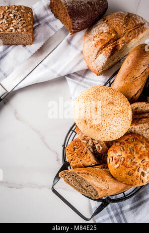 Auswahl an frischen, hausgemachten Korn Brot, in einem Metallkorb, weißem Marmor Background Copy space Stockfoto