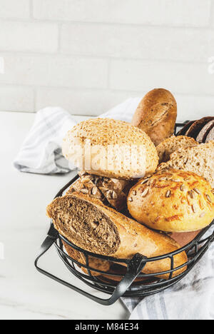 Auswahl an frischen, hausgemachten Korn Brot, in einem Metallkorb, weißem Marmor Background Copy space Stockfoto