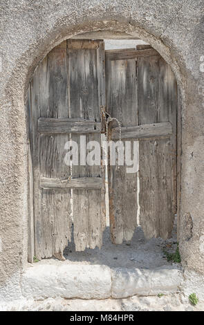 607 Emborio. Eine alte staubige Tür ich die Straßen von emborio auf Santorini, mit einem modernen Breeze Block und Kunststoff Flasche auf dem Boden Stockfoto