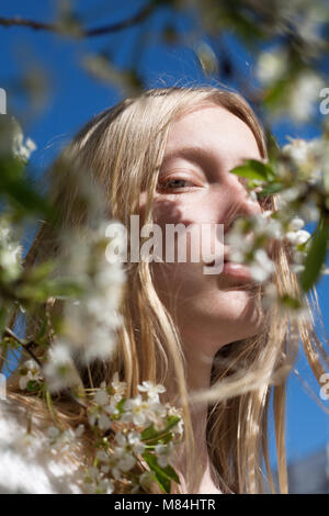 Hübsches blondes Mädchen im Frühling Blumen und blauer Himmel Stockfoto