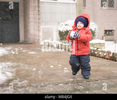 Baby Boy, während es schneit läuft mit einem Schneeball in seinen Händen Stockfoto