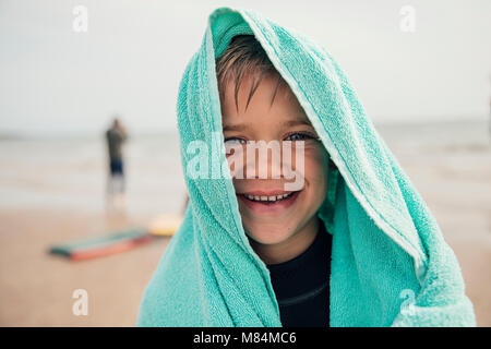 Kleiner Junge in ein Handtuch eingewickelt nach dem Surfen am Strand. Stockfoto