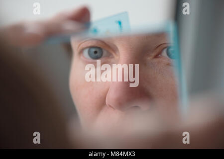 Frau Zupfen der Augenbrauen mit Pinzette durch die Fenster, selektiver Fokus Stockfoto