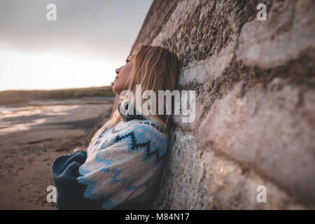 Frau lehnte sich gegen die Wand an einem Strand Stockfoto