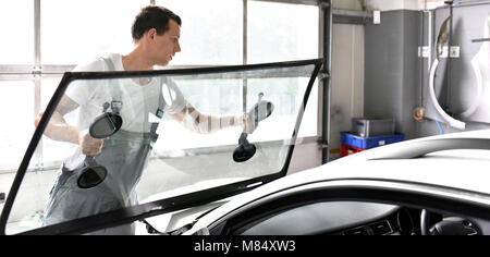Mechaniker in der Garage ersetzt defekte Windschutzscheibe eines Autos Stockfoto