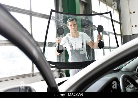 Mechaniker in der Garage ersetzt defekte Windschutzscheibe eines Autos Stockfoto