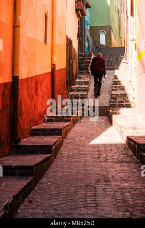 Ein einsamer mexikanische Mann zu Fuß die engen, kopfsteingepflasterten Gasse in zwischen bunten Häuser in Guanajuato, Mexiko Stockfoto