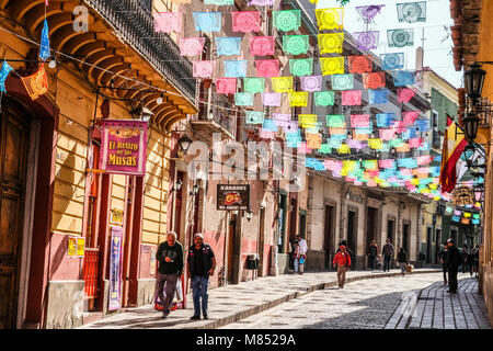 Mexikaner zu Fuß auf der Straße mit Kopfsteinpflaster mit Sonne beleuchtet bunte Banner Flaggen oben auflegen Stockfoto