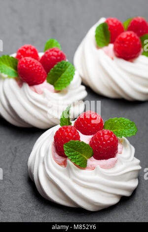 Mini Pavlova meringue Nester mit Himbeeren und Minze auf schwarzen Stein Hintergrund Stockfoto