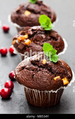 Triple Chocolate Muffins mit Preiselbeeren auf schwarzen Stein Hintergrund Stockfoto