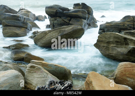 Moody Beach Bild von glatten nassen Felsen mit fließenden verschwommen Wasser bei Tageslicht Stockfoto