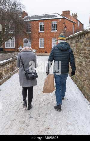 Der Mann und die Frau zu Fuß auf einem Pfad in Schnee und Eis bedeckt der Mann trägt eine Einkaufstasche, beide trugen Woolly Pom Pom bobble hats Stockfoto