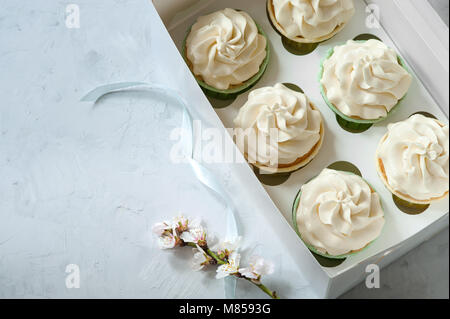 Vorliegenden Konzept. Frische, weiße Blumen und Geschenk Box mit Cupcakes auf Holztisch. Platz für die Beschriftung. Muttertag, Liebhaber' Tag, Geburtstag Stockfoto