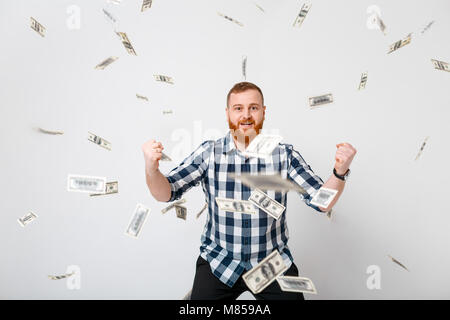 Junge schöne glücklicher Mann mit dem roten Bart stehen unter Geld Regen der Dollarscheine Stockfoto