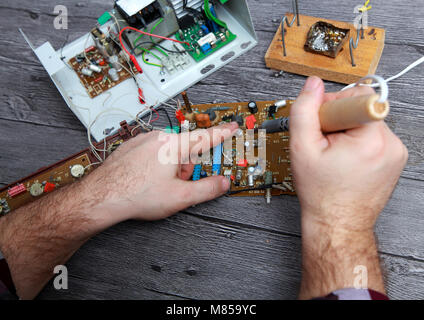 Der Master auf Reparatur der Radio elektronische Ausrüstung entfernt die Betriebsprämienregelung aus dem elektronischen Gerät. Master ändern Sie das Teil mit einem Lötkolben Stockfoto