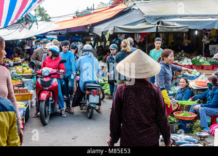 Menschen und Motorroller konkurrieren um Raum zu einem Markt im Freien auf einer Straße in Hoi An, Vietnam Stockfoto