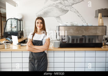 Kaffee Business Owner Konzept - Portrait von Happy attraktiven jungen schönen kaukasischen Barista in Schürze Kamera im Coffee shop Zähler lächelnd. Stockfoto