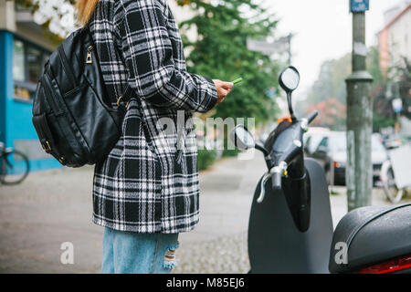 Ein Tourist mit einem Rucksack wird eine elektrische Scooter durch eine mobile Anwendung auf dem Telefon verwenden und distal zu aktivieren. Ein beliebtes Fahrzeug in Stockfoto
