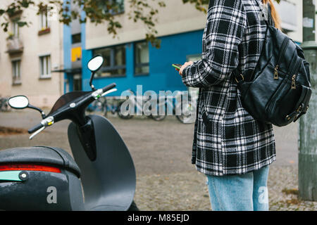 Ein Tourist mit einem Rucksack wird eine elektrische Scooter durch eine mobile Anwendung auf dem Telefon verwenden und distal zu aktivieren. Ein beliebtes Fahrzeug in Stockfoto