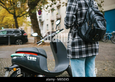 Ein Tourist mit einem Rucksack wird eine elektrische Scooter durch eine mobile Anwendung auf dem Telefon verwenden und distal zu aktivieren. Ein beliebtes Fahrzeug in Stockfoto